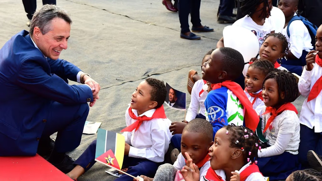 Bundesrat Ignazio Cassis sitz bei einer Afrikareise mit Kindern aus der Region am Boden und lacht.