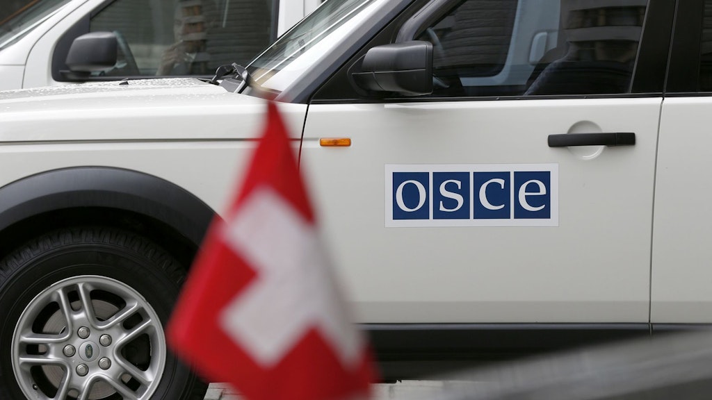 Ein weisser Geländewagen mit der Aufschrift «OSZE» steht vor einem schwarzen Wagen auf welchem die Schweizer Flagge angebracht ist.
