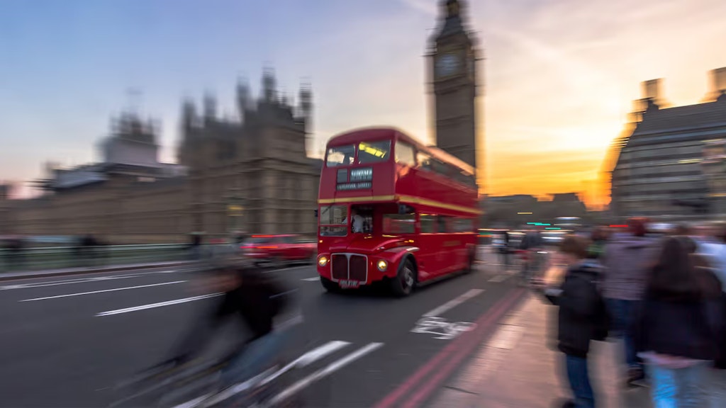 Ein für London typischer roter Doppeldeckerbus fährt vorbei am Big Ben über die Westminster Bridge ins Abendrot. 