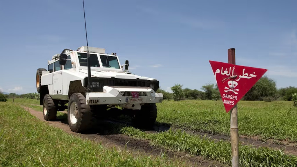 Ein Minenräumungsfahrzeug im Einsatz auf einem Feld, auf dem ein Schild auf das Vorhandensein von Minen hinweist.