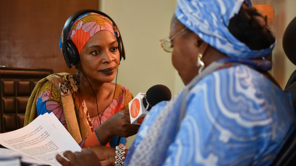 Eine afrikanische Frau interviewt mit einem Mikrofon in einem Radiostudio eine andere Frau.