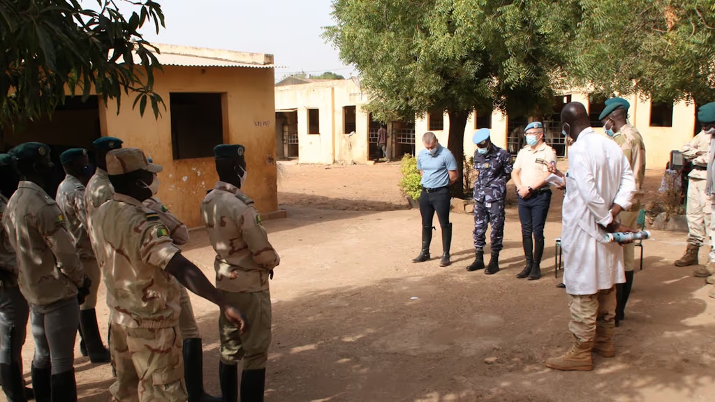 Carl Emery, begleitet von einem malischen Gendarmeriekommandanten in Tracht, steht vor neun uniformierten Offizieren.