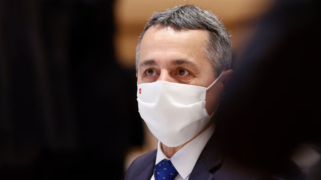 Nahaufnahme von Bundesrat Ignazio Cassis wie er im Rahmen einer UNO-Versammlung im November 2020 im Saal sitzt und eine Gesichtsmaske mit Schweizerkreuz trägt. 