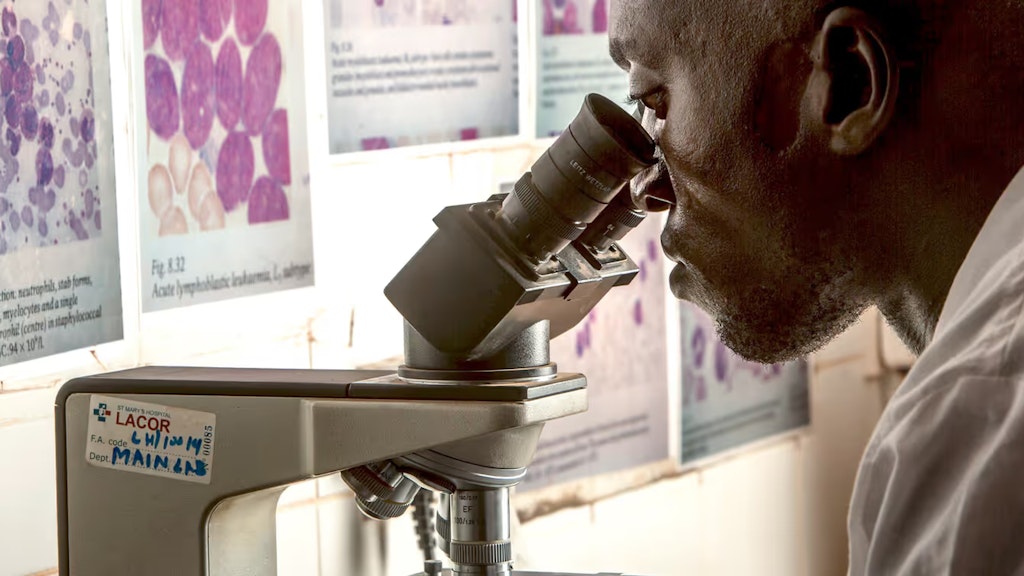 Ein Mitarbeiter in einem Spital blickt durch ein Mikroskop.