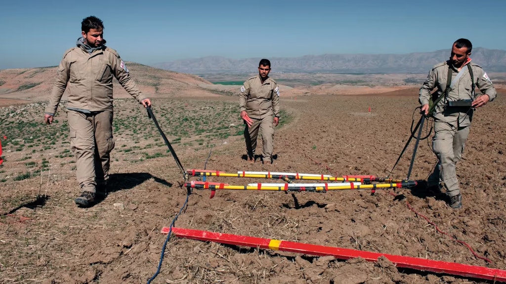 Drei Männer in Overalls räumen ein Feld in der irakischen Wüste.