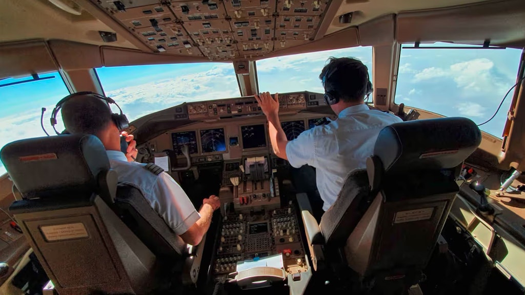 Zwei Piloten im Cockpit eines Flugzeugs. Unter ihnen liegt das Wolkenmeer. 