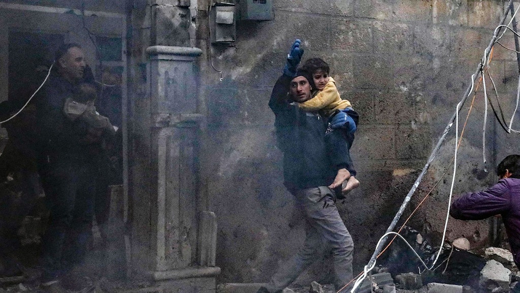 Ein Mann hält inmitten von Trümmern in Syrien ein Kind in den Armen.