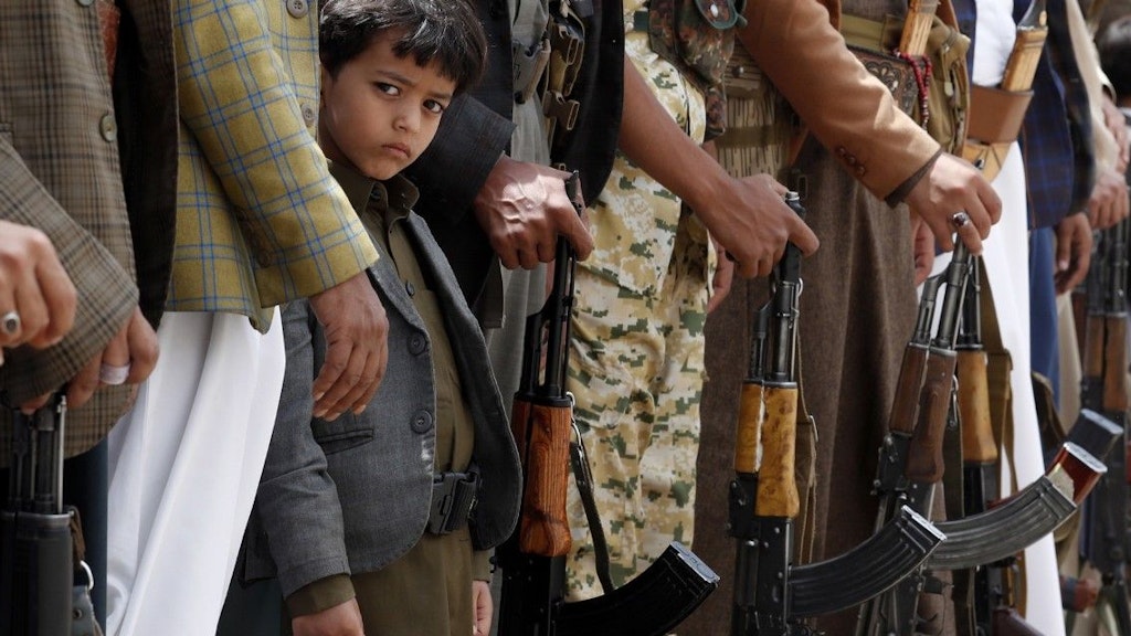 Ein jemenitischer Junge steht zwischen Erwachsenen, die Gewehre vor sich halten.