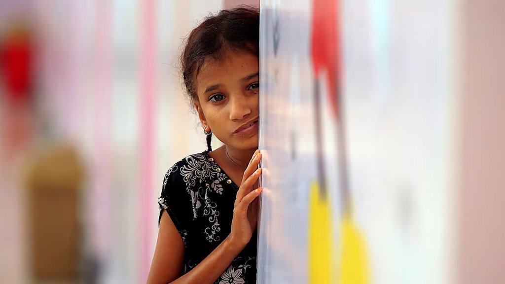 Ein kleines Mädchen lehnt mit besorgtem Gesichtsausdruck an einer Wand und wartet darauf, Essen zu bekommen.