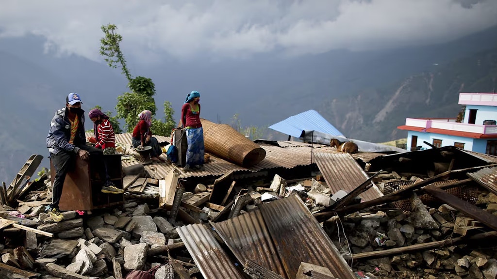 Eine nepalesische Familie mit zwei Kindern sitzt auf den Trümmern ihres Hauses in einem Dorf in den Bergen.