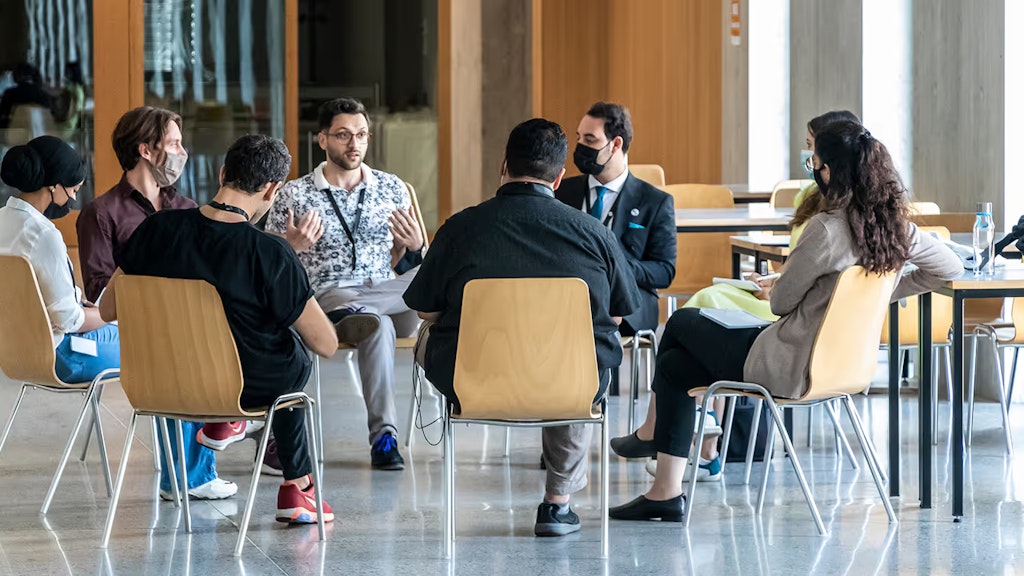 Einige Teilnehmer des MEM Summer Summit diskutieren, während sie auf Stühlen im Kreis sitzen.