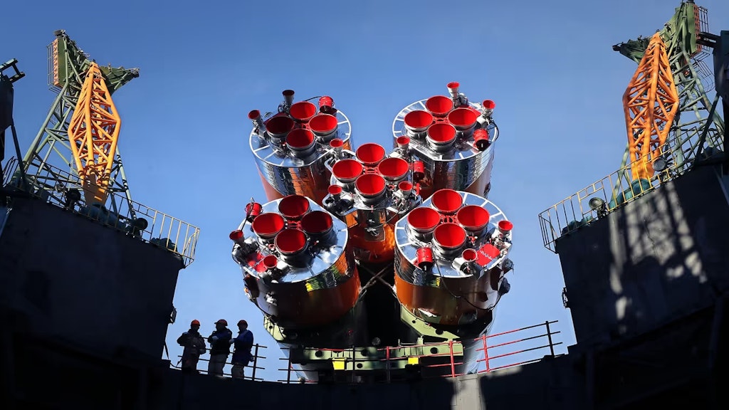 Das Triebwerk einer Rakete neben einer Abschussrampe bei stahlblauem Himmel.