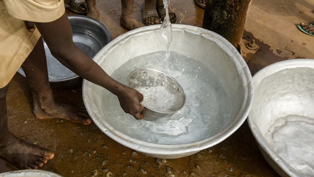 Mehrere Personen stehen an einem Brunnen und schöpfen mit einer Schale sauberes Wasser. 