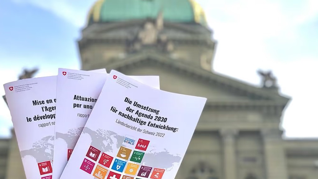 Im Vordergrund drei Exemplare des Länderberichts in verschiedenen Sprachen. Im Hintergrund das Bundeshaus.