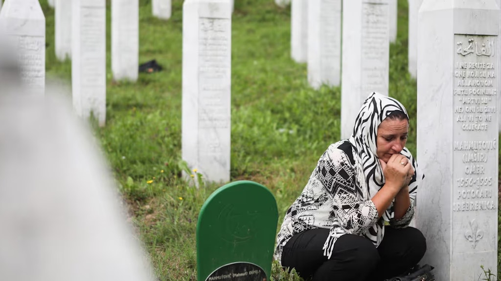 Eine Frau kniet neben einem Gedenkstein auf dem Friedhof in Srebrenica.