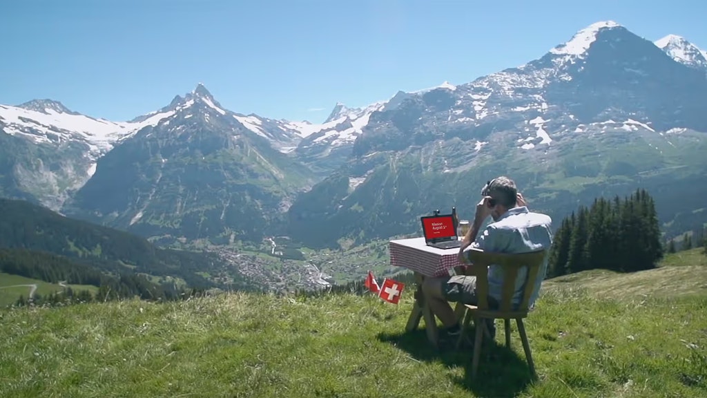 Ein Mann sitzt in den Alpen an einem Tisch und arbeitet am Laptop.