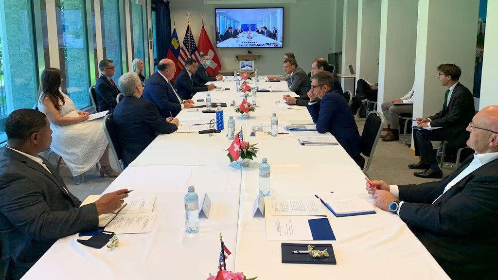 Mehrere Personen an einem Konferenztisch in der Schweiz diskutieren über eine Videokonferenz mit Kollegen in Amerika.