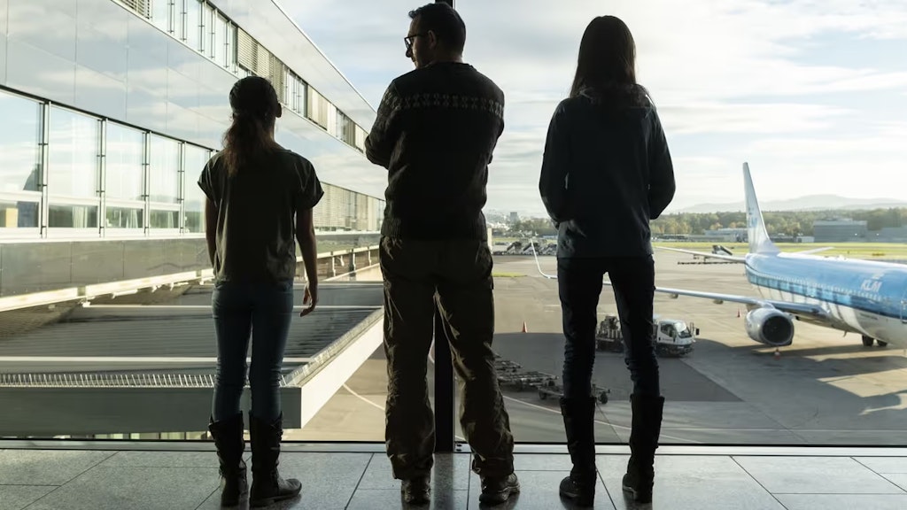Am Flughafen stehen zwei Kinder mit einer erwachsenen Person am Fenster