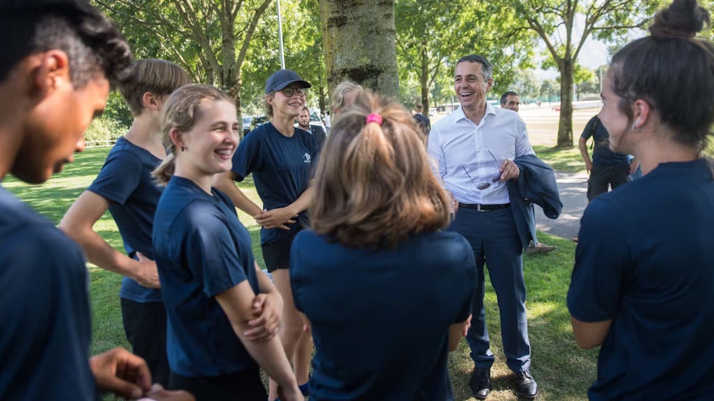 Bundesrat Ignazio Cassis im Gespräch mit Leichtathletinnen und Leichtathleten beim Training. 