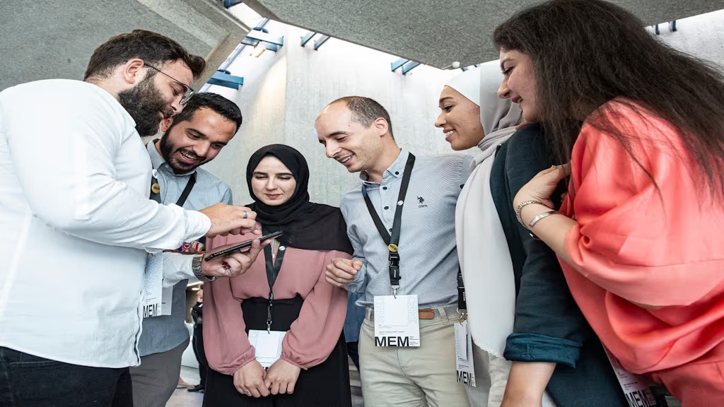 Im Halbkreis stehende junge Erwachsene blicken auf das Display eines Telefons.