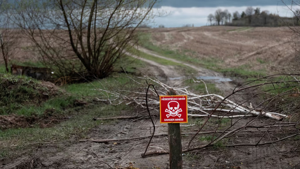 Ein rotes Schild mit einem Totenkopf steht auf einem Weg und warnt vor einem Minenfeld.