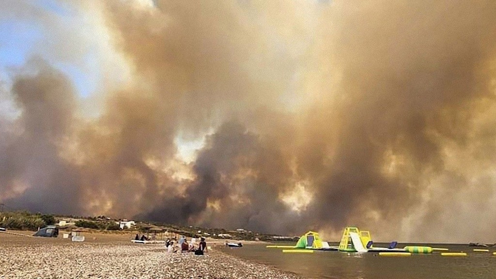 Ein Kiesstrand mit Rutschbahnen und Luftmatratzen, über dem dichte Rauchwolken aufsteigen.