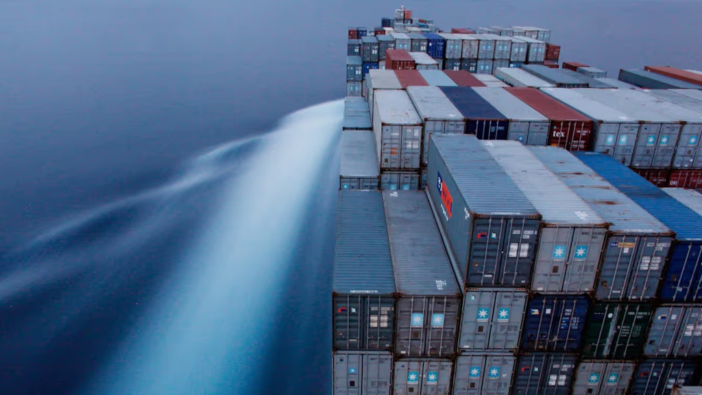 Ein Frachter transportiert zahlreiche Container. Im Hintergrund, Wasser.
