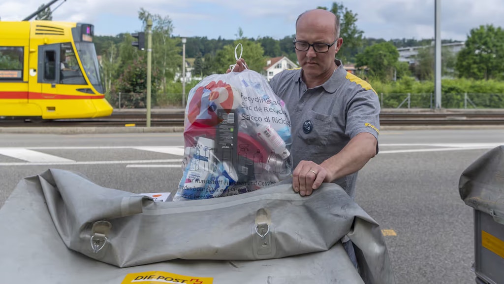 Ein Pöstler verstaut einen Recycling-Sack mit leeren Kunststoffflaschen und Getränkekartons in seinem Karren. 