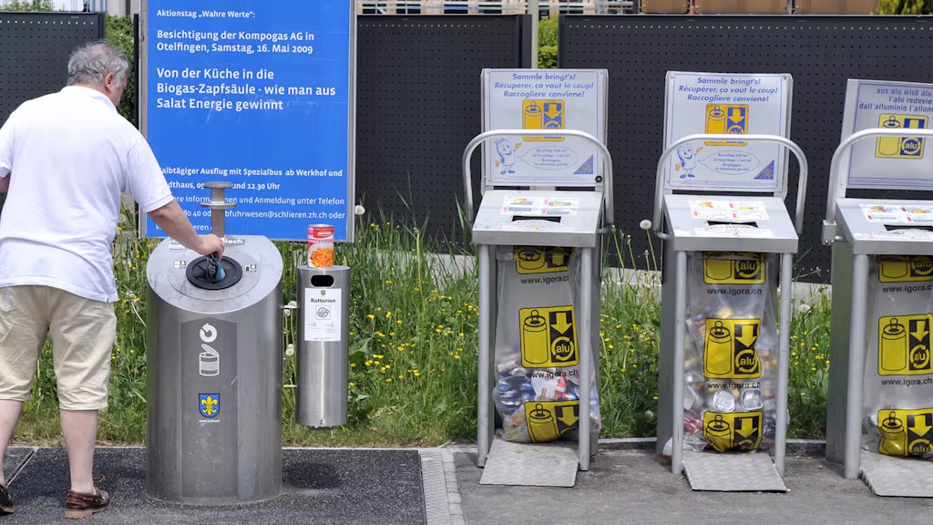 Ein Mann entsorgt eine Büchse Weissblech. Zudem sind drei Sammelstellen für Aluminium-Getränkedosen zu sehen.