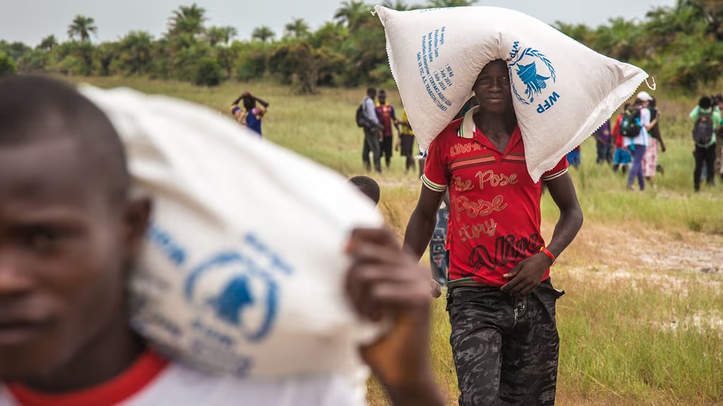Zwei Männer tragen Säcke mit Nahrungsmitteln auf Schultern und Kopf.