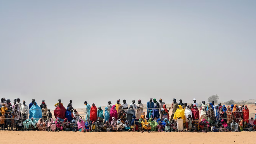 Eine Gruppe von Menschen steht in einer Reihe hinter einem Zaun.