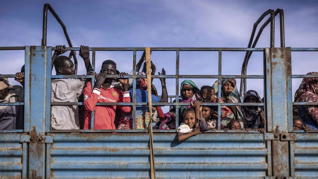 Sudanesische Frauen, Männer und Kinder stehen eng zusammen auf der Ladefläche eines blauen Lastwagens.