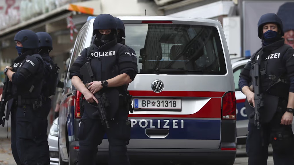 Mehrere schwer bewaffnete österreichische Polizisten stehen vor einem Polizeiauto.