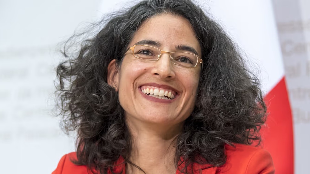 Porträt von Corinne Cicéron Bühler, lächelnd mit der Schweizer Fahne im Hintergrund.