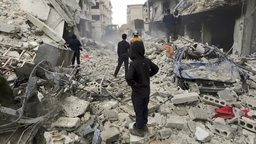 In einer Strasse in der Stadt Idlib gehen Zivilisten durch ein Trümmerfeld. Im Vordergrund schaut ein vermummter Junge in die Ferne.