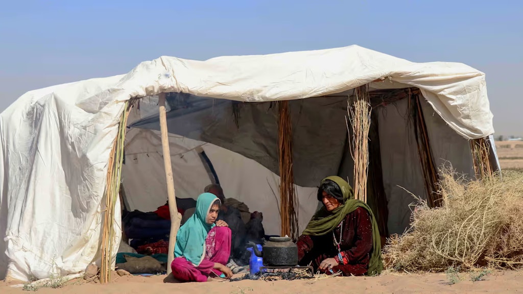 Eine Frau und ein Mädchen sitzen unter einem provisorischen Zeltdach in der Wüste.