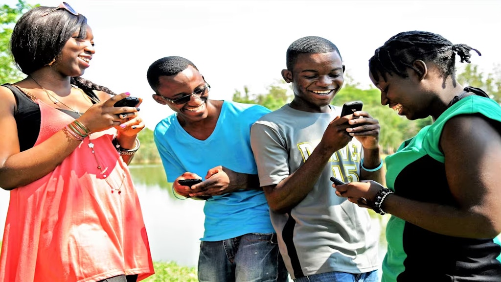 Vier Jugendliche schauen lachend auf die Bildschirme ihrer Mobiltelefone.