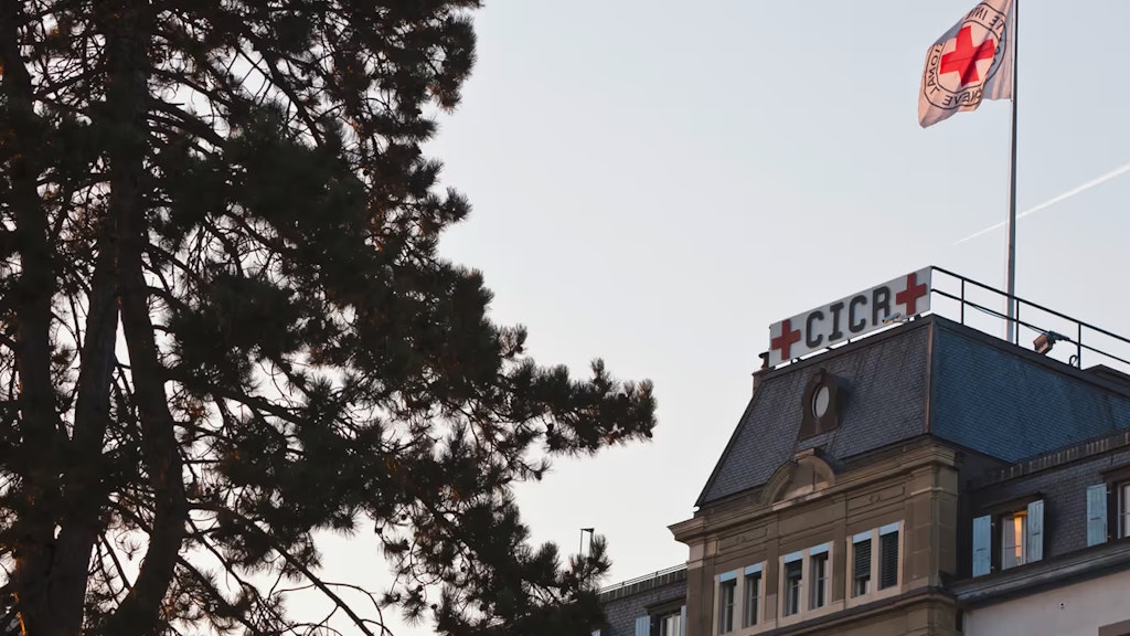 Eine Tafel und eine Flagge auf dem Dach des IKRK zeigen das bekannte Emblem der humanitären Organisation: ein rotes Kreuz auf weissem Grund.