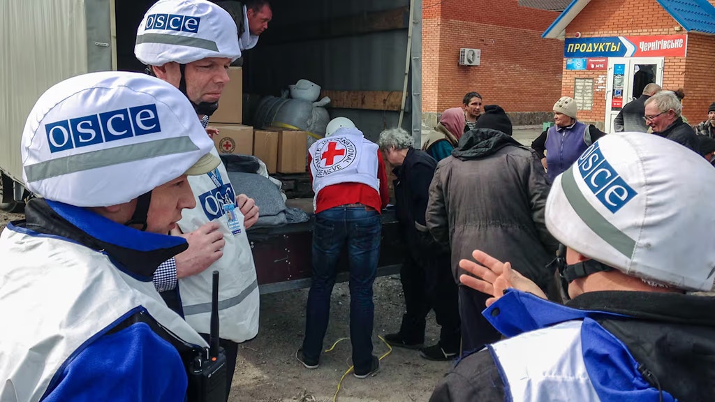 Drei Mitglieder der OSZE-Mission beobachten die Verteilung von Hilfspakten an die Bevölkerung.