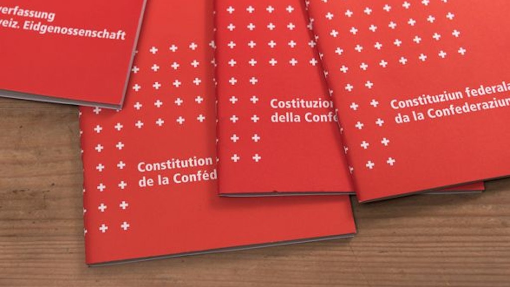 Copie della Costituzione federale svizzera nelle quattro lingue nazionali su una superficie in legno.