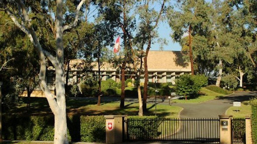 The Swiss embassy building set in a garden with a Swiss flagpole and a large tree in the foreground.