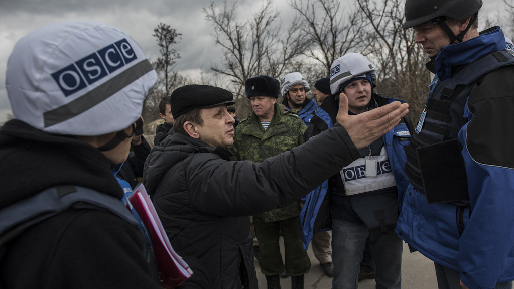 OSCE Personal im Gespräch mit einem Mann in der Ukraine. Draussen.