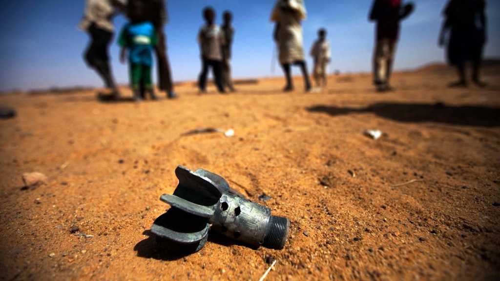 25 marzo 2014 Alcuni bambini guardano i resti di un proiettile di mortaio che giacciono nella sabbia dopo gli scontri nel campo Alabassi per sfollati interni a Mellit, nel Darfur settentrionale.