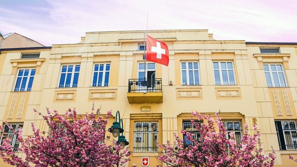 A building with a Swiss flag and two trees in the foreground, the Swiss embassy.
