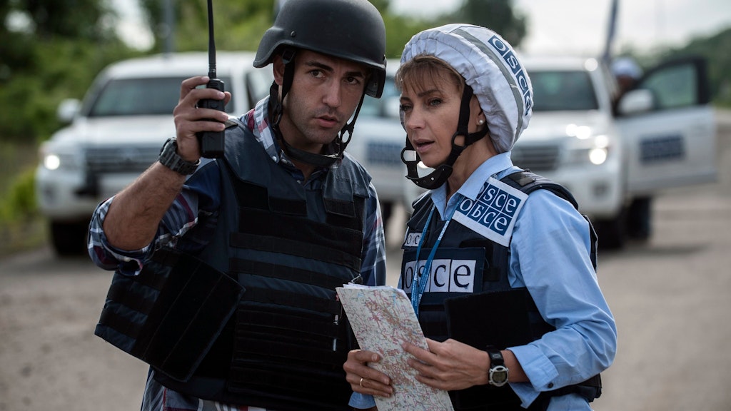 Ein Mann und eine Frau mit Karte und Funk besprechen sich. Beide tragen Schutzausrüstung und Helm. Die Frau ist mit OSCE angeschrieben.