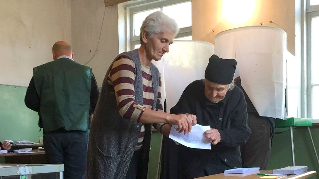 Due donne davanti a un’urna elettorale durante le elezioni locali in Georgia. Si aiutano a vicenda a piegare una scheda elettorale nel locale adibito a seggio.