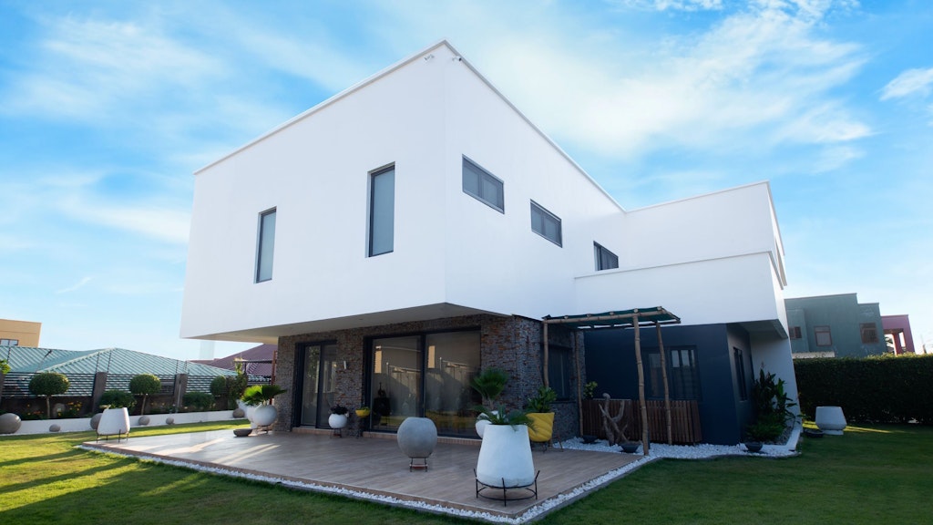 A white, modern-looking house with a terrace and garden.