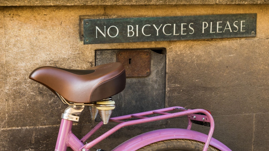A pink bike against a wall with a sign reading ‘No bicycles please’ in capital letters.