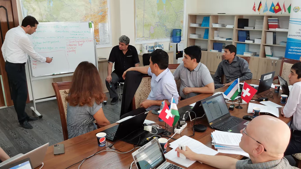 Frauen und Männer schauen auf eine weisse Wandtafel und folgen den Erklärungen eines Mannes.