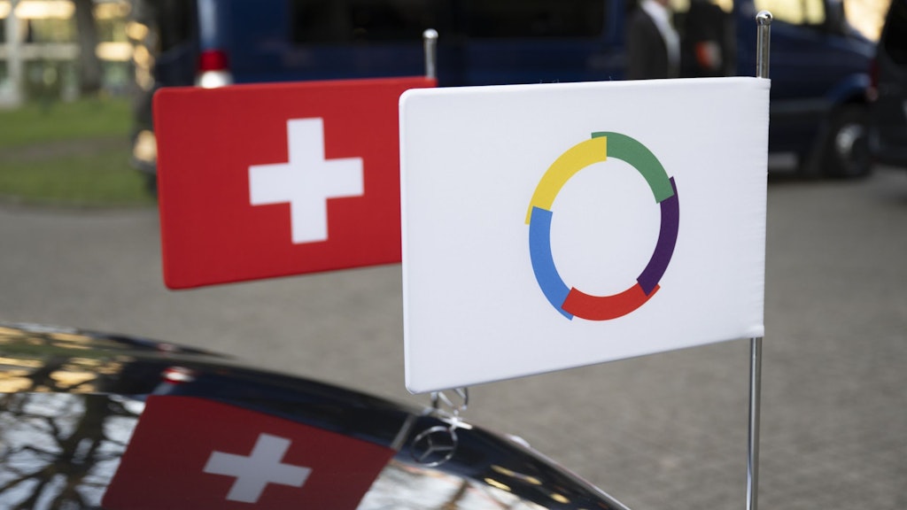 La photo montre les drapeaux de l'Organisation internationale de la Francophonie (OIF) et de la Suisse accrochés à une voiture.
